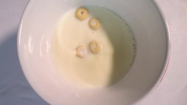 Müsli halkalarını bir tabağa doldurmak süt, üst görüş, tabakta yemek kahvaltısı, yavaş çekimde döner döner döner döner döner döner döner. Yakın plan..