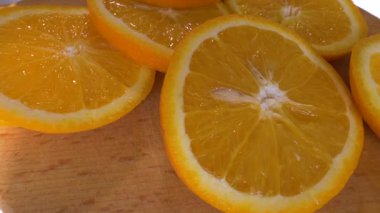 Tahta kesme tahtasında dönen portakal dilimleri. Meyve portakalı halka şeklinde kesilmiş. Ağır çekim. Yakın plan.