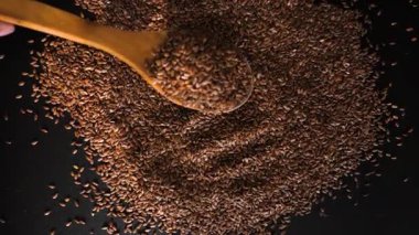 Tahta bir kaşıktan masaya keten tohumu dök. Keten tohumlarını ağır çekimde siyah bir masaya dökün.