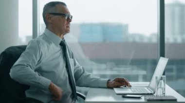 yaşlı işadamı modern ofisindeki bilgisayarla çalışma. Sırtı ağrıyor olduğunu