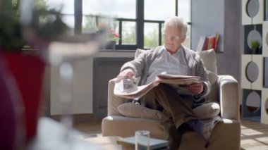 yaşlı adam bir sandalyede oturur ve modern bir dairede bir gazete okuma