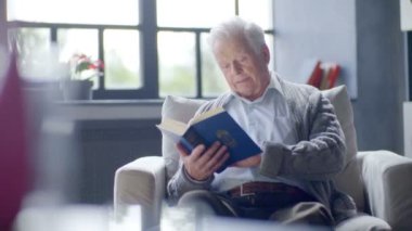 yaşlı beyaz adam bir kitap okuma ve modern bir dairede lezzetli bir çay içme