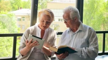 Mutlu çift ayakta birbirimizi karşısında tablet ve kitap ile güzel emekli. Onlar gülümseme.