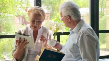 Mutlu çift ayakta birbirimizi karşısında tablet ve kitap ile güzel emekli. Onlar gülümseme.