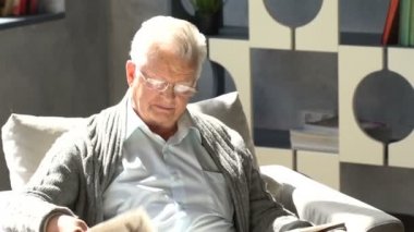 mutlu yaşlı adam bir sandalyede oturur ve modern bir dairede bir gazete okuma