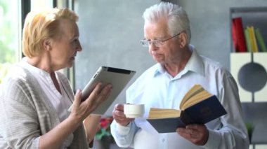 Mutlu çift ayakta birbirimizi karşısında tablet ve kitap ile güzel emekli. Onlar gülümseme.