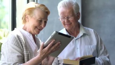 Mutlu çift ayakta birbirimizi karşısında tablet ve kitap ile güzel emekli. Onlar gülümseme.