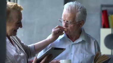 Mutlu çift ayakta birbirimizi karşısında tablet ve kitap ile güzel emekli. Onlar gülümseme.