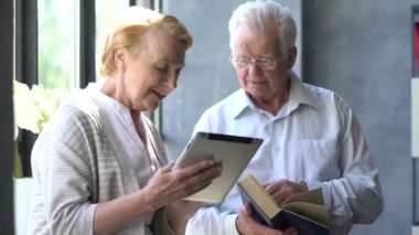 Mutlu çift ayakta birbirimizi karşısında tablet ve kitap ile güzel emekli. Onlar gülümseme.