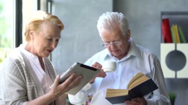 Mutlu çift ayakta birbirimizi karşısında tablet ve kitap ile güzel emekli. Onlar gülümseme.