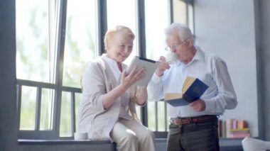 Mutlu çift ayakta birbirimizi karşısında tablet ve kitap ile güzel emekli. Onlar gülümseme.