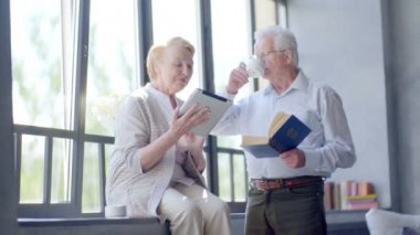 Mutlu çift ayakta birbirimizi karşısında tablet ve kitap ile güzel emekli. Gülümseme ve içecek çay