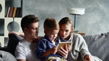 Çocuğuyla birlikte tablet evde koltukta oturan genç mutlu çift