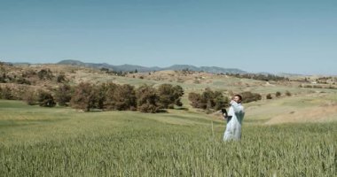 Kendini adamış bir kadın yemyeşil bir tarlada filizlenen mahsulleriyle ilgilenir, doğanın güzelliğini gösterir.