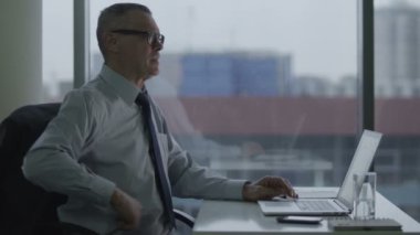 yaşlı işadamı modern ofisindeki bilgisayarla çalışma. Sırtı ağrıyor olduğunu