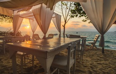 Deniz ve kumsal beyaz masa seti ve sabah güneşiyle aydınlanan beyaz kumaş..