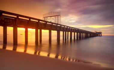 Gün batımında uzun deniz köprüsü Ilık, düşük aydınlık ve karanlık gölgelerle.