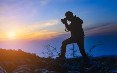 DSR kameralı siluet fotoğrafçı dağın tepesinde gün batımı gökyüzü.