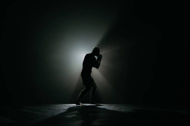 Dövüşçü bir darbe vuruyor. Profesyonel spor. Dövüşmek. Kuvvet. Karamsar bir ışık ve tahıl ruh hali içinde bir savaşçı. Koyu renk spor salonunda boksör eğitimi.