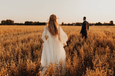 Gün batımında güzel bir tarlada düğün çifti. Buğday tarlasında gün batımı ışığı. Yeni evliler. Aşk konsepti. Düğün konsepti