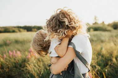 Anne-kız ilişkisi. Anne çocuğuna sarılıyor. Anne ve kızı güzel bir tarlada yürüyor.
