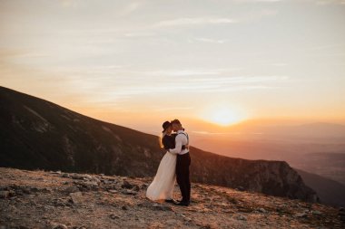 Gün batımında dağın tepesinde duran güzel bir çift.