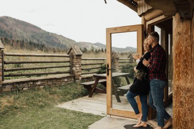 Bir çift sabah kahvesi içip, tahta dağın evinde öpüşüyor.