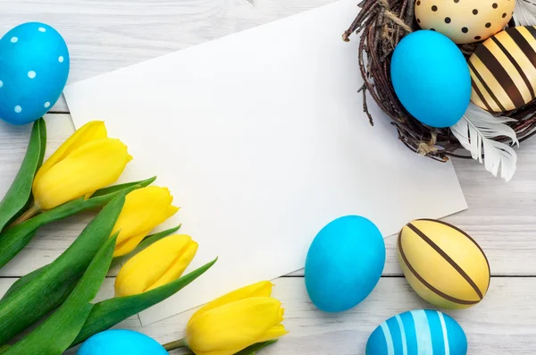 Beyaz ahşap bir zemin üzerinde paskalya yumurtası ve laleleri logo ya da metin için bir kart.