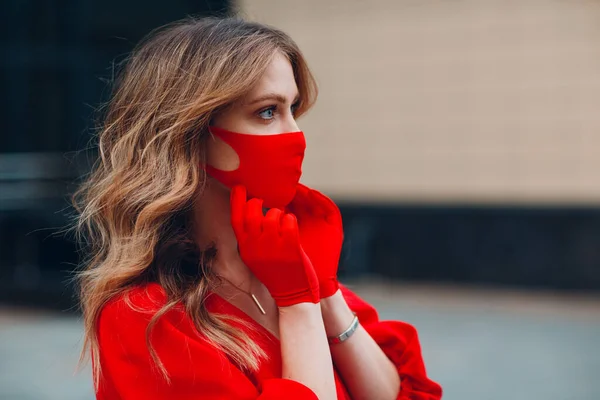 Junge Frau in rotem Kleid und Handschuhen setzt medizinische Gesichtsmaske auf — Stockfoto