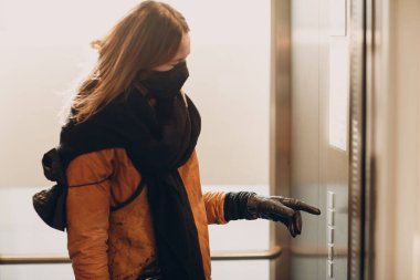 Coronavirus pandemik covid-19 karantina konsepti sırasında eldiven ve işaret parmağıyla asansöre basan tıbbi maskeli kadın.