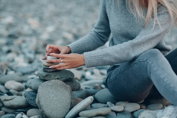 Young woman builds stone stacks pyramid on pebble beach