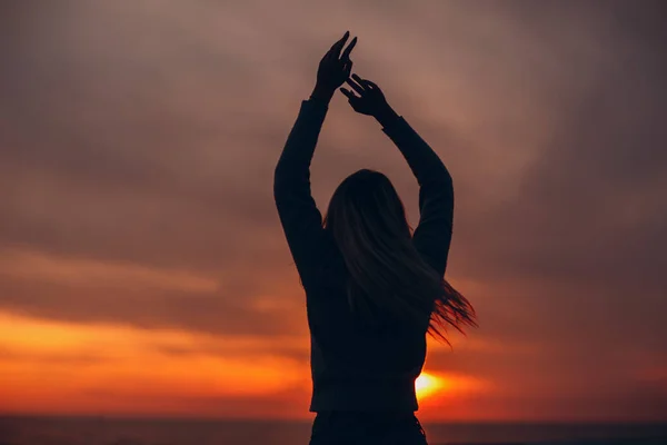Silhouette giovane donna sulla riva del mare con le mani in alto. — Foto Stock