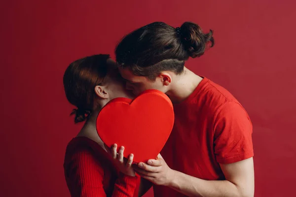 Hombre y mujer joven pareja besándose y escondiéndose detrás de una caja en forma de corazón — Foto de Stock