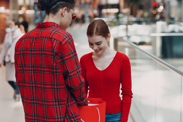 Un tipo le da a su novia una caja en forma de corazón en el Día de San Valentín. Pareja joven en el centro comercial. —  Fotos de Stock