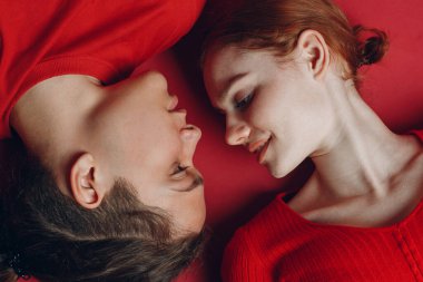 Yerde eğlenen iki genç insan. Bir çift aşık erkek ve kadın kırmızı arka planda yatıyor..