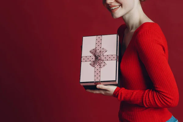 Wanita berambut merah memegang kotak hadiah merah muda dengan pita. Latar belakang merah potret potret gambar studio — Stok Foto