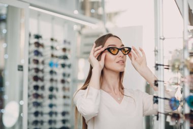 Alışveriş merkezinin gözlükçü köşesinde gülümseyen ve bardakları seçen muhteşem genç bayanı yakından çek. Optometriste gözlük alan mutlu güzel bir kadın.
