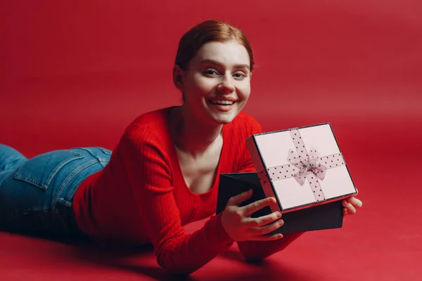 Happy gembira wanita memegang hadiah kotak hadiah hadir. Cute mengejutkan gadis di latar belakang merah. Valentines hari — Stok Foto