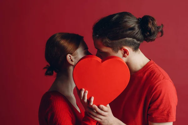 Homem e mulher jovem casal beijando e se escondendo atrás de caixa em forma de coração — Fotografia de Stock