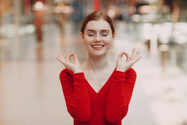 Potret wanita muda yang tersenyum dengan mata tertutup di pusat perbelanjaan. Yoga, tenang, zen dan konsep meditasi pada pandemia covid-19 — Stok Foto