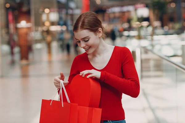 Concepto del Día de San Valentín. Mujer joven con bolsas de compras y retrato de caja en forma de corazón rojo en la tienda del centro comercial —  Fotos de Stock