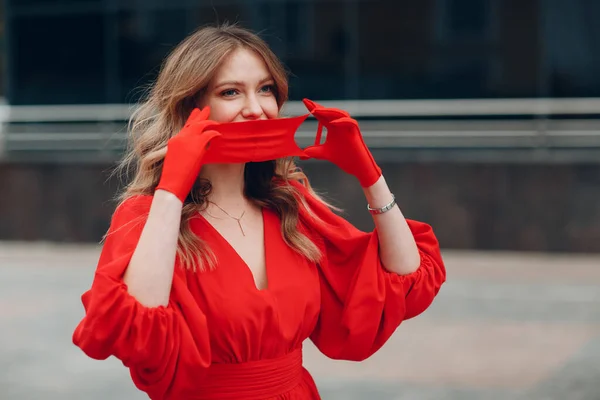 Молодая женщина в красном платье и перчатках надевает медицинскую маску для лица — стоковое фото