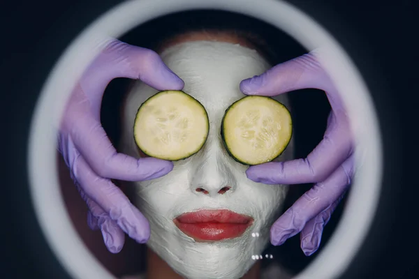 年轻美丽的女人在温泉美容院接受脸上带黄瓜的黏土面罩 — 图库照片