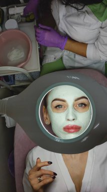 Genç bir kadın güzellik merkezinde yüzüne kilden bir maske takıyor.