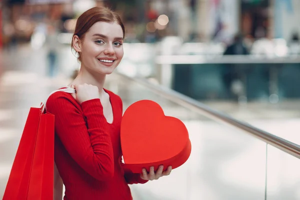 Concepto del Día de San Valentín. Mujer joven con bolsa de compras y retrato de caja de regalo en forma de corazón rojo en la tienda del centro comercial —  Fotos de Stock