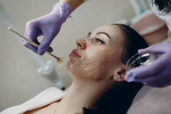 Esteticista aplicando com gel de contato escova no rosto da mulher para procedimentos de hardware no spa de beleza — Fotografia de Stock