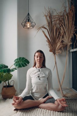 Yetişkin bir kadın evde yoga yapıyor. Bilgisayarında online dersler var.