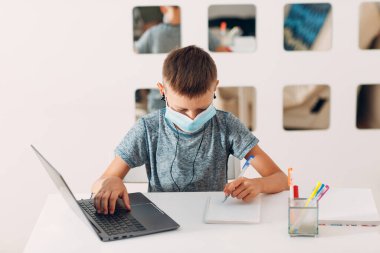 Kulaklık takan, laptoplu, tıbbi maskeli ve okula hazırlanan genç bir çocuk. Çevrimiçi eğitim kavramı.
