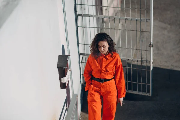 Junge Häftlingsfrau im orangefarbenen Anzug beim Rauchen im Gefängnis. Weibchen in bunten Overalls. — Stockfoto