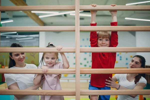 Kids doing Swedish wall exercises in gym at kindergarten or elementary school. Children sport and fitness concept.